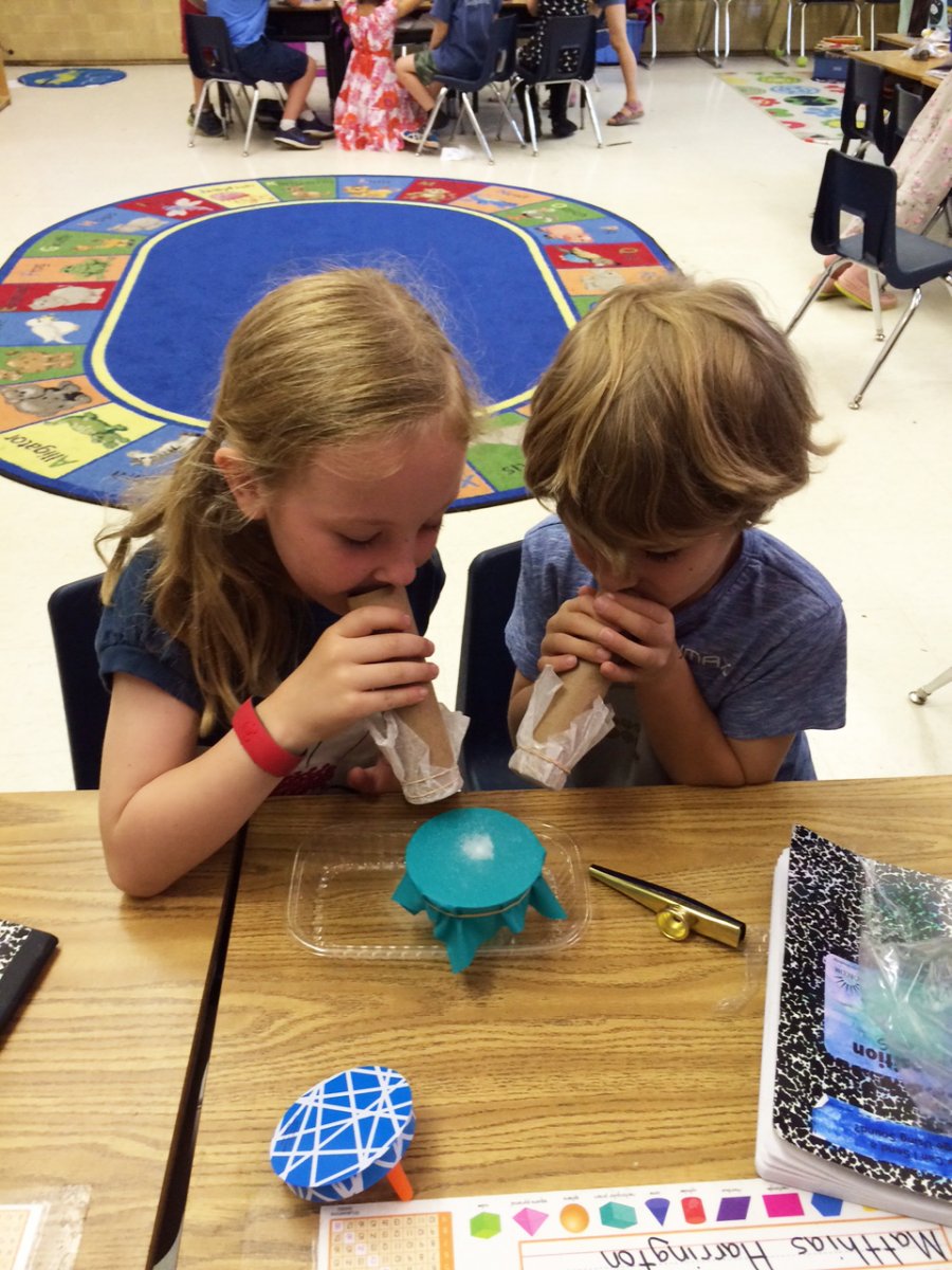 Two students playing kazoos and watching the effect on salt sitting on top of a stretched rubber sheet.