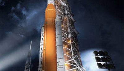 Photo of the a large orange rocket on a launch pad at night with lights shining on it.