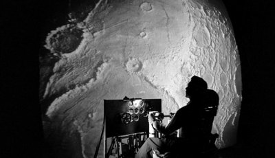 Large image of the Moon with a person in a chair looking at the image and a computer screen