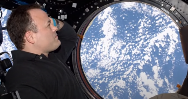 Astronaut in the Space Station looking out a window down onto Earth.