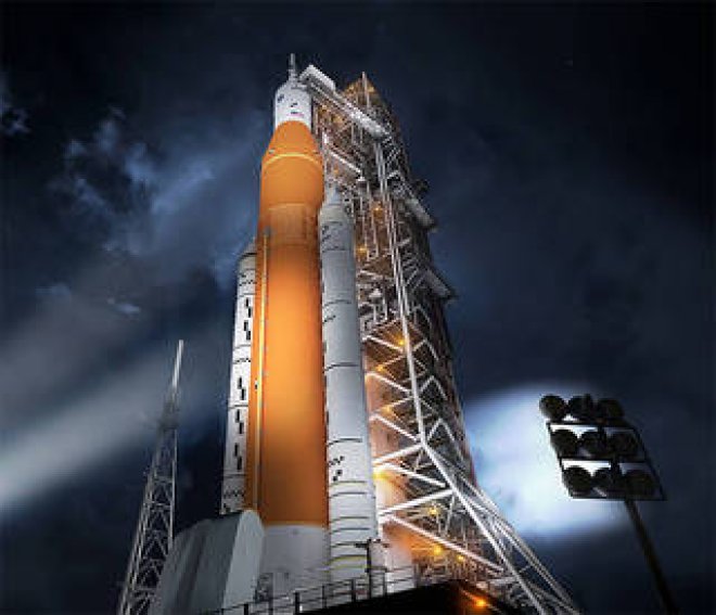 Photo of the a large orange rocket on a launch pad at night with lights shining on it.