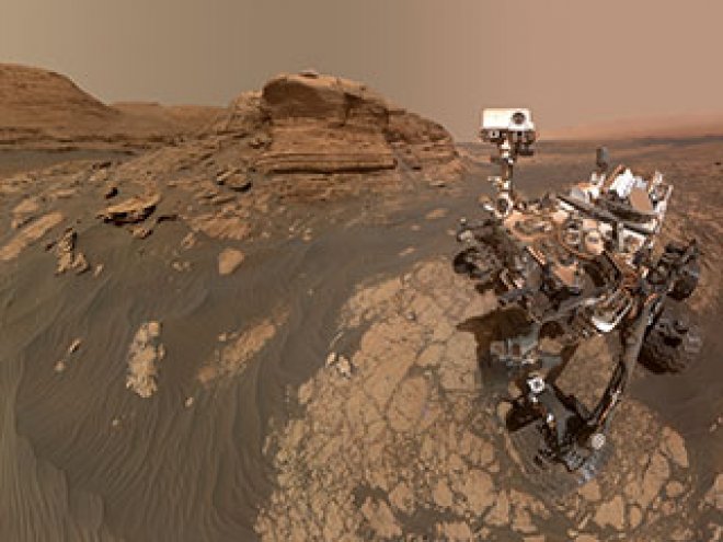 Image of the Martian surface of reddish dust and rock and the rover on the right hand side.